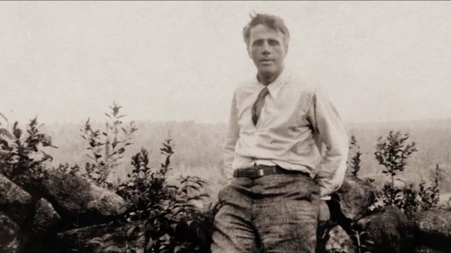 Black and white photo of Robert Frost posing against a landscape