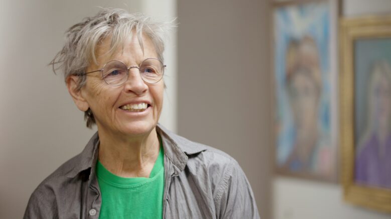 Eileen Myles smiles while wearing a green shirt and gray jacket